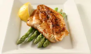 A perfectly seasoned fish fillet rests on a bed of asparagus, a lemon wedge on the side. A delightful dish inspired by Spanish fish recipes.