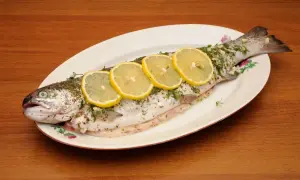 A whole trout, seasoned and garnished with lemon slices and herbs, ready to be cooked as trucha a la navarra.