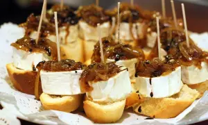 Delicious pincho recipes: bite-sized bread topped with creamy cheese, caramelized onions, and a balsamic glaze, all secured with a toothpick.