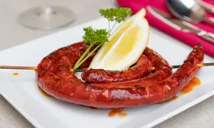 A coiled chistorra sausage, grilled to perfection, served on a white plate with a lemon wedge and parsley. A delicious chistorra recipe.