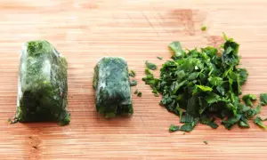 Learn how to freeze fresh herbs: two frozen herb blocks and a pile of chopped herbs on a wooden cutting board.