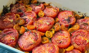 A baking dish filled with juicy, slow roasted tomatoes and cherry tomatoes, seasoned with herbs and spices.