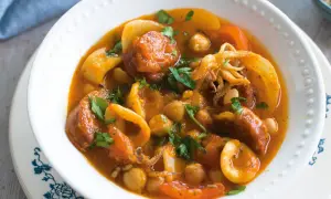 A hearty Spanish stew with tender squid rings, chickpeas, and chorizo in a rich tomato sauce, garnished with fresh parsley.