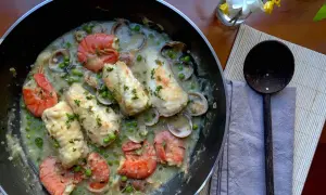 A delicious bonito fish recipe with prawns, clams, and peas in a creamy sauce, garnished with parsley.