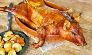 A whole roasted suckling pig, golden brown and glistening, sits in a rustic clay dish. This image evokes delicious suckling pig recipes and a feast.