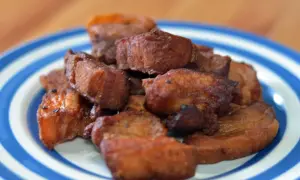 A pile of crispy fried pork belly, or chicharrones, on a blue and white striped plate.