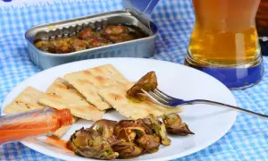 A fork lifts a smoked oyster from a plate of crackers, a bottle of hot sauce and a beer nearby. Delicious smoked oyster recipes are easy to make with these ingredients.