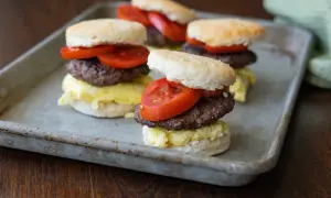 Fluffy biscuits layered with scrambled eggs, a savory goose sausage patty, and fresh tomato slices.