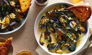 A delicious bowl of moules marinière, brimming with plump mussels in a creamy broth, served with crusty bread and a glass of beer.