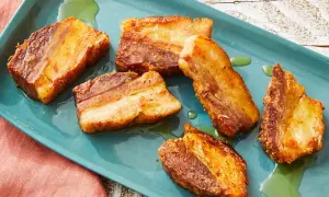 Crispy pork belly, Spanish style, glistening on a teal platter with a hint of green oil.