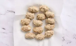 A dozen uncooked croquetas de pollo are arranged on white parchment paper, ready for frying.
