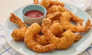 Crispy fried shrimp piled high on a plate, with a small bowl of red dipping sauce.