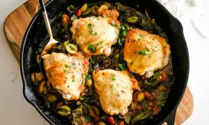 Four golden chicken thighs nestled in a rich, rustic chicken basque stew with olives and peppers, garnished with fresh parsley.