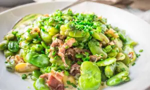 A delicious dish showing how to cook fava beans with bacon and chives, served in a creamy sauce on a white plate.