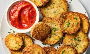 Crispy spanish fried eggplant slices, golden brown and seasoned, served with a side of vibrant tomato sauce and sprinkled with fresh parsley.