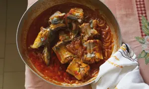 A rustic pan of eel recipes, featuring chunks of eel simmered in a rich, tomato-based sauce with onions.