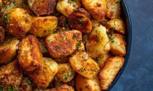 Crispy, golden-brown roasted new potatoes, seasoned with herbs and spices, piled high in a dark blue bowl.