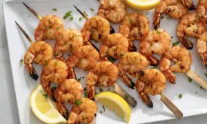 A platter of perfectly grilled shrimp skewers, seasoned and garnished with fresh parsley and lemon wedges.