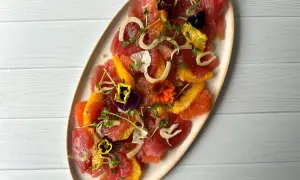A vibrant tuna crudo dish featuring thinly sliced raw tuna, citrus segments, fennel, microgreens, and edible flowers.