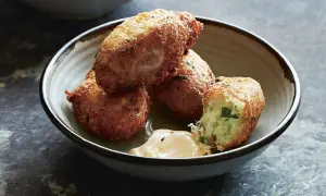 Golden-brown croquetas de bacalao, one broken open to reveal a fluffy interior, sit in a rustic bowl with a dollop of creamy sauce.