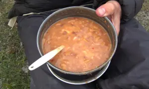 A hearty bowl of gulas fish stew, served in a metal pot with a white spoon, ready for a meal outdoors.