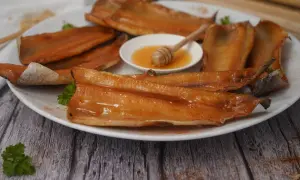 A plate of glistening smoked trout fillets, with a small dish of honey and a honey dipper. A delicious start to any meal.