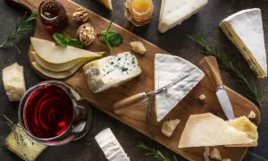 A beautiful spread of wine and cheese pairings, featuring a glass of red wine, various cheeses, pears, walnuts, and honey on a wooden board.