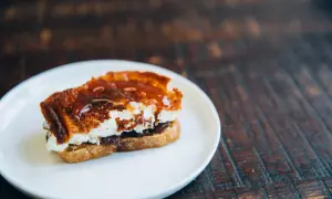 A decadent goat cheese toast, caramelized and drizzled with a rich, glossy sauce, sits on a white plate.