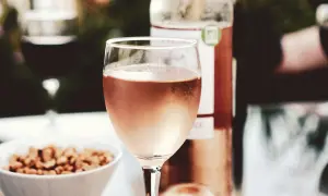 A glass of rosé wine, perhaps a Marsanne blend, sits on a table with a bowl of nuts and a bottle of wine.