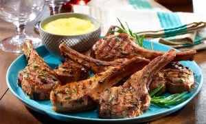 Grilled lamb chops, seasoned with rosemary, served on a blue plate with a side of yellow sauce. A taste of Spanish lamb meat.