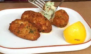 Golden brown cod fritters served with a dollop of mashed potatoes and a lemon wedge. A fork is lifting a bite of the fritter.