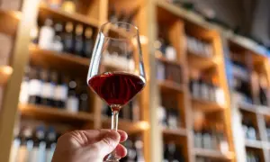 A hand holds a glass of red wine, with shelves of wine bottles in the background. Some believe certain red wines may boost metabolism.