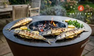 Four whole grilled fish, stuffed with lemon and herbs, sizzle on a round barbecue grill over glowing coals.