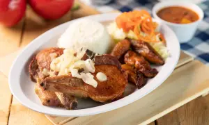 A delicious plate of chuleta meat, a flavorful pork chop, served with rice, fried plantains, salad, and beans.