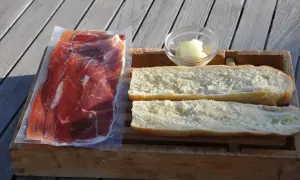 Ingredients for a delicious jamon iberico sandwich: thinly sliced cured ham, buttered bread rolls, and a small dish of butter.