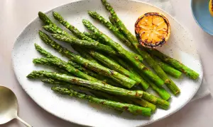 A plate of perfectly grilled spanish asparagus, lightly charred and served with a grilled lemon slice.