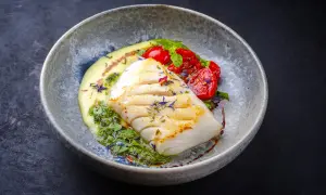 A beautifully plated poached fish recipe, featuring a white fish fillet with grilled marks, served with creamy sauce, pesto, and cherry tomatoes.