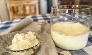 A small glass bowl overflows with fluffy crème fraîche, next to a jar of the creamy dairy product.