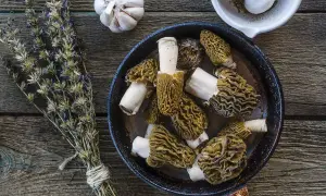 A pan of wild asparagus mushrooms, garlic, and dried herbs on a wooden table, ready for a delicious meal.