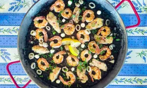 A delicious squid ink rice paella, brimming with plump shrimp, tender calamari rings, and flaky white fish, all garnished with fresh green onions and lemon wedges.