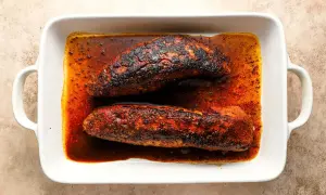 Two seasoned pork tenderloins, ready for a delicious solomillo recipe, rest in a white baking dish filled with rich, spiced juices.