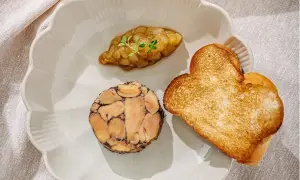 A slice of duck terrine with a dollop of compote and heart-shaped toast on a scalloped plate.