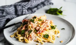 A plate of creamy smoked salmon pasta, garnished with fresh basil and pine nuts.