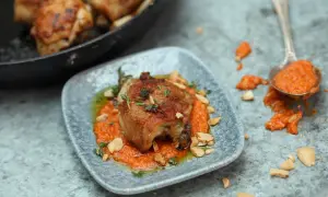 A succulent piece of chicken, part of a delicious chicken tapas dish, rests on a bed of vibrant orange sauce, garnished with herbs and chopped nuts.