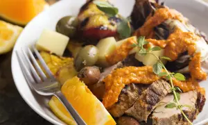 Slices of grilled spanish pork tenderloin with olives, orange wedges, and a vibrant romesco sauce.