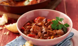 A hearty bowl of Spanish beef dishes, featuring tender beef chunks, beans, and peppers in a rich, savory sauce, garnished with fresh parsley.