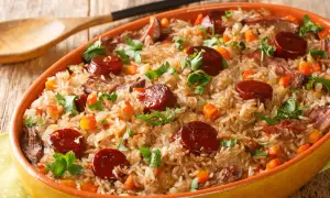 A hearty dish of rice with sauteed chorizo, tender meat, and diced carrots, garnished with fresh parsley.