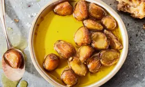 Golden garlic cloves swimming in olive oil, a delicious result of how to make garlic confit. A spoon holds one tender clove.