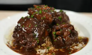 Tender, braised oxtail pieces in a rich, dark sauce, served over fluffy white rice and garnished with chopped green onions. A delicious oxtail recipe.