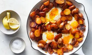 Huevos rotos: a hearty skillet dish with fried eggs nestled among crispy, golden-brown potato slices, served with lemon wedges and sea salt.
